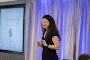 Allison Shapira delivering a keynote on human-centered leadership in a tech-driven world, with a smile and expressive gesture