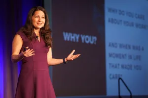 Allison Shapira delivering a keynote on authentic communication with the words “WHY YOU?” projected behind her