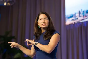 Allison Shapira speaking on stage, gesturing with both hands during a presentation.
