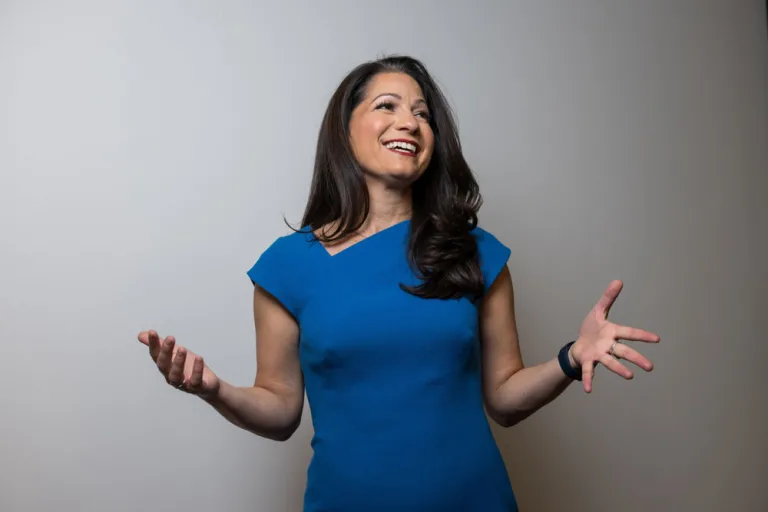 (Allison Shapira) Speaker in blue dress smiling and gesturing while presenting on leadership and influence