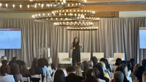 Allison Shapira delivering a keynote presentation to a live audience, demonstrating audience engagement and effective public speaking.