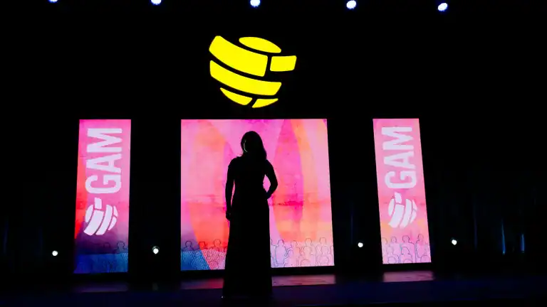Allison Shapira stands in silhouette on a darkened conference stage against illuminated pink panels.